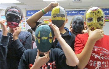 group of students holding handmade masks up to their faces